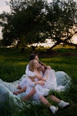 A circle of women sitting outdoors, holding hands in a serene forest clearing at sunset.