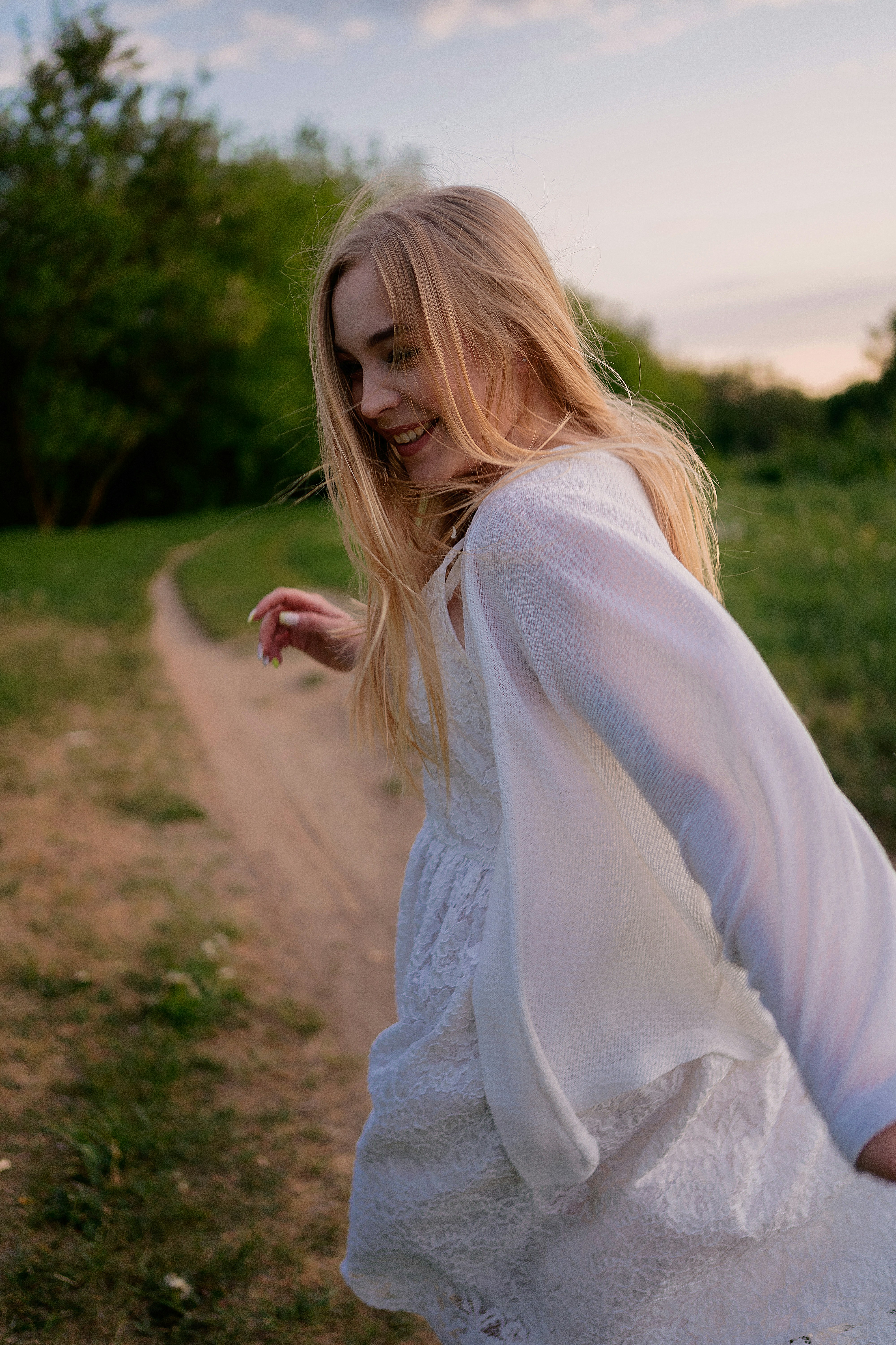 a woman in a white dress walking down a dirt road