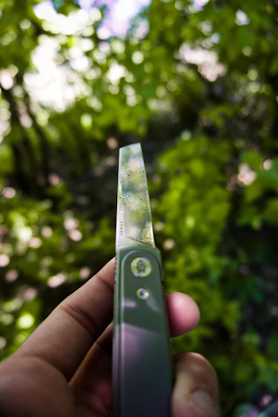 Close-up of a hand holding a handcrafted bushcraft knife against a backdrop of green forest.