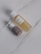 Two cosmetic bottles are placed on a light marble surface. One is a transparent bottle filled with a yellow liquid and has a white cap, labeled as botanical calendula oil. The other is a smaller pump bottle with a brown base and white top.