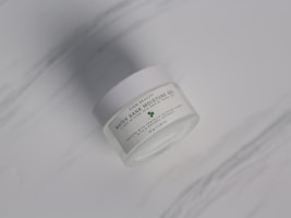 A sleek glass jar of hydrating moisturizer with droplets of water on the surface.