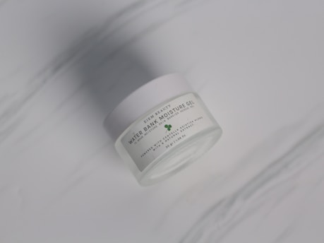 A sleek glass jar of hydrating moisturizer with droplets of water on the surface.