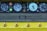 An industrial control panel features several large round dials with numbers and needle indicators. Adjacent are colored buttons, including bright red and green. The panel sits above a flat textured surface, and a row of rounded knobs is aligned at the bottom, all against a yellow background.