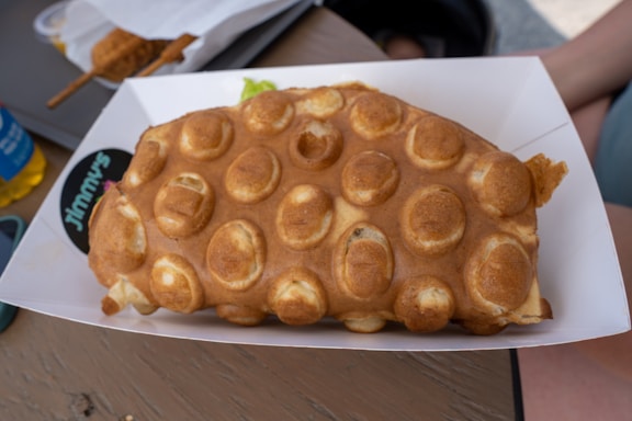 A colorful display of bubble waffles topped with fresh fruit and drizzled chocolate on a rustic wooden table.