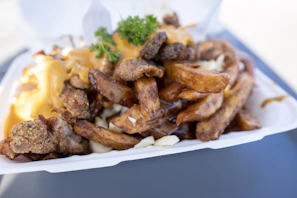 A vibrant butter chicken poutine topped with fresh herbs, served on a rounded cream-colored plate