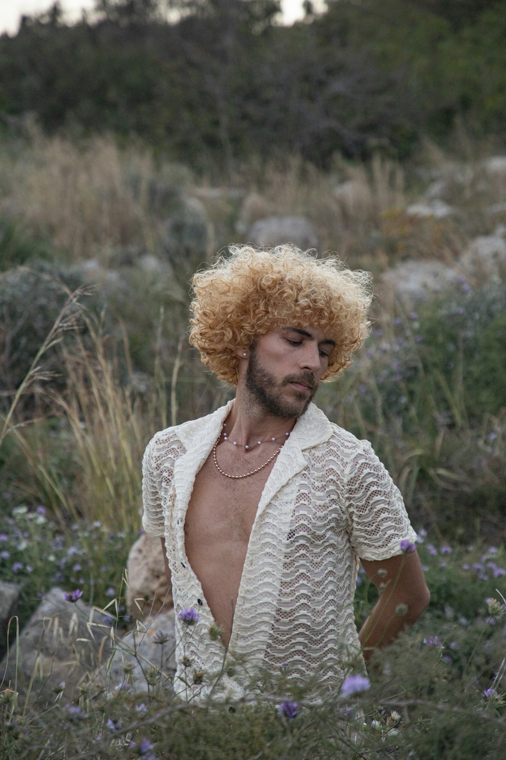a man with curly hair standing in a field