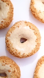 Several donuts with a creamy glaze and crumb topping are arranged against a white background. Each donut has a light brown, golden crumb coating with a smooth, glossy glaze on top.