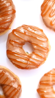 Delicious-looking doughnuts with a glossy caramel glaze and a drizzle of caramel sauce. They are arranged on a white surface, highlighting their shiny texture and appetizing appearance.