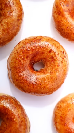 Several golden-brown, freshly baked bagels arranged in a close-up view against a clean, white background. The bagels have a shiny, glazed surface, indicating they might be freshly out of the oven.