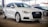 A sleek, white Audi car is parked in a covered area, with other vehicles visible in the background. The car is positioned at an angle, showcasing its front and side profile. The environment suggests a dealership or showroom setting with ample lighting.