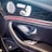 The image features the interior door panel of a luxury car, showcasing a sleek and modern design. It includes an elegant combination of materials such as leather and wood grain finish. Visible elements include a high-quality speaker with chrome accents, seat adjustment buttons, and a window control panel.