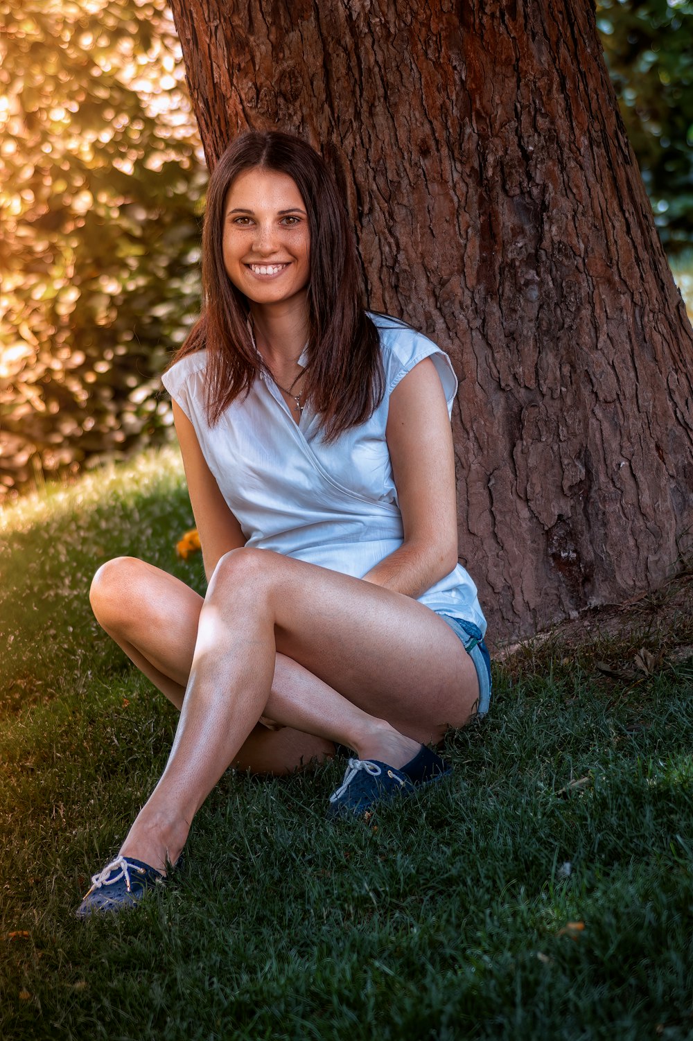 a woman sitting in the grass next to a tree