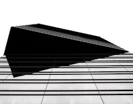 A modern architectural structure with a sharp, geometric design. The building features a series of parallel lines that create a sense of depth and complexity. The high contrast between the black elements and the white background emphasizes the clean, minimalist style.