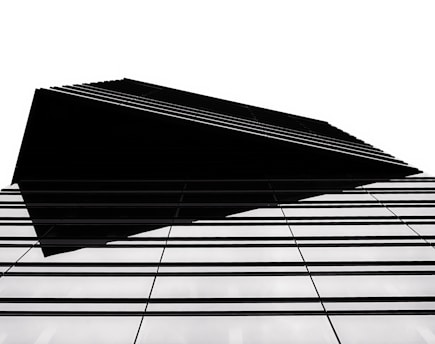 A modern architectural structure with a sharp, geometric design. The building features a series of parallel lines that create a sense of depth and complexity. The high contrast between the black elements and the white background emphasizes the clean, minimalist style.