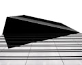 A modern architectural structure with a sharp, geometric design. The building features a series of parallel lines that create a sense of depth and complexity. The high contrast between the black elements and the white background emphasizes the clean, minimalist style.
