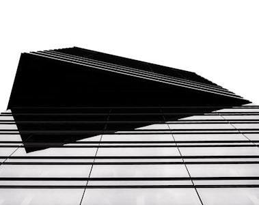 A modern architectural structure with a sharp, geometric design. The building features a series of parallel lines that create a sense of depth and complexity. The high contrast between the black elements and the white background emphasizes the clean, minimalist style.
