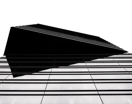 A modern architectural structure with a sharp, geometric design. The building features a series of parallel lines that create a sense of depth and complexity. The high contrast between the black elements and the white background emphasizes the clean, minimalist style.