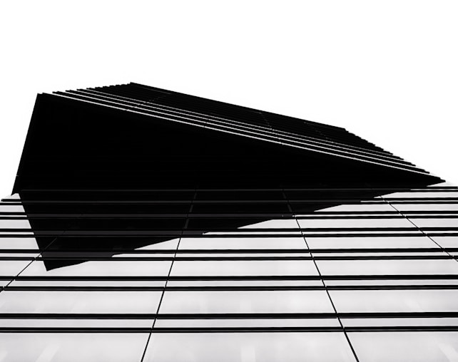 A modern architectural structure with a sharp, geometric design. The building features a series of parallel lines that create a sense of depth and complexity. The high contrast between the black elements and the white background emphasizes the clean, minimalist style.