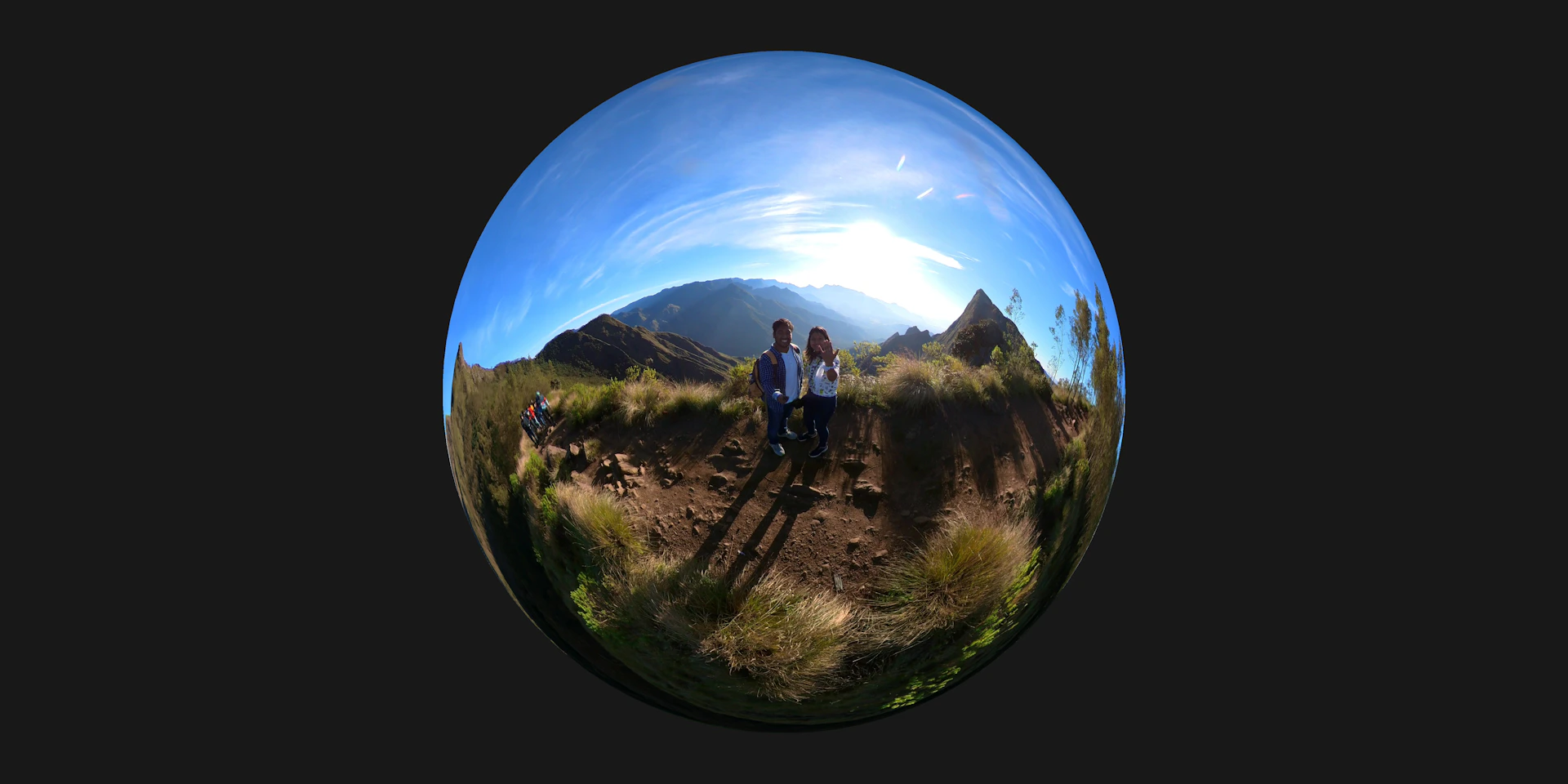 A panoramic mountain view with a winding trail where a couple pauses to admire the scenery.