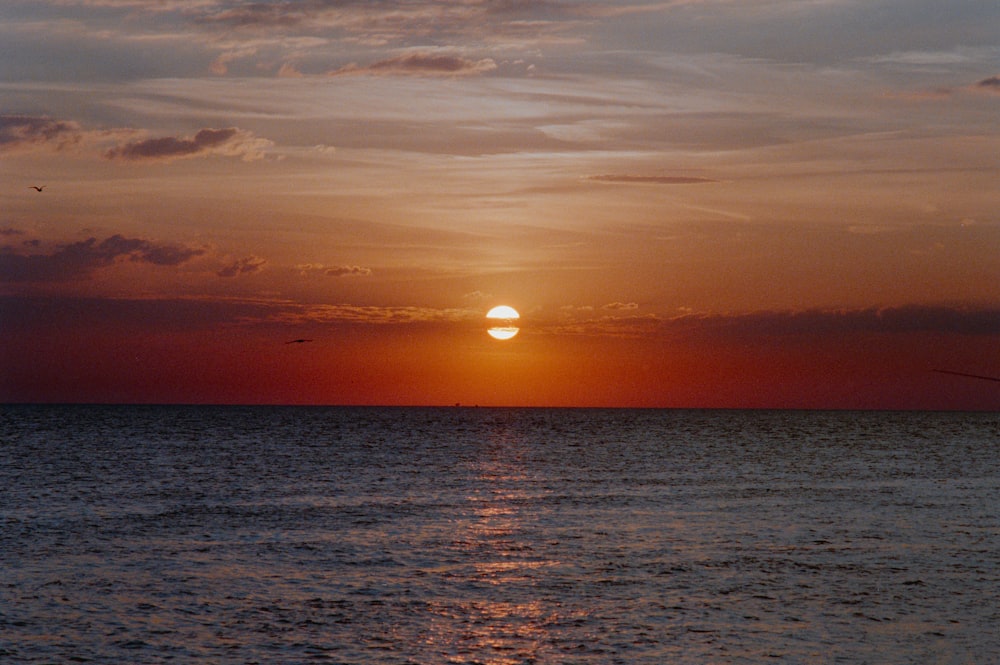 the sun is setting over the ocean with birds flying in the distance