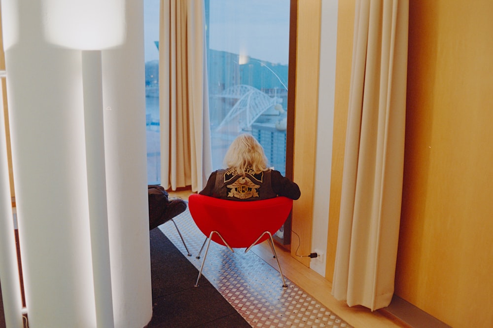 a woman sitting in a red chair looking out a window