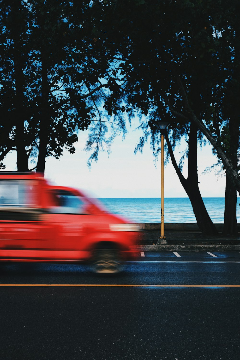 a red car driving down a street next to the ocean
