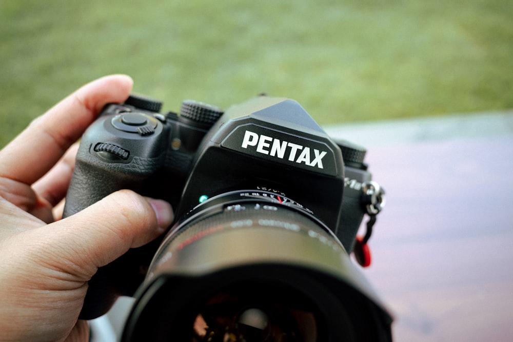 a person holding a camera with a pentax lens