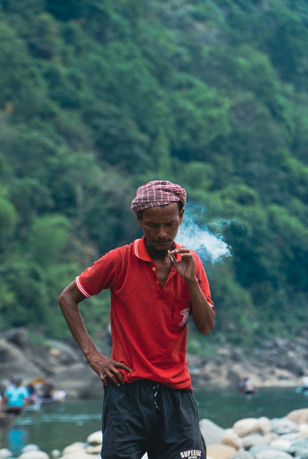 a man standing next to a river smoking a cigarette