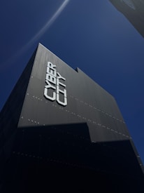 A tall, modern building is captured from a low angle against a clear blue sky. The facade of the building reads 'CYBER CITY' in large, bold letters. The building's surface appears sleek and dark, with minimal reflective features.