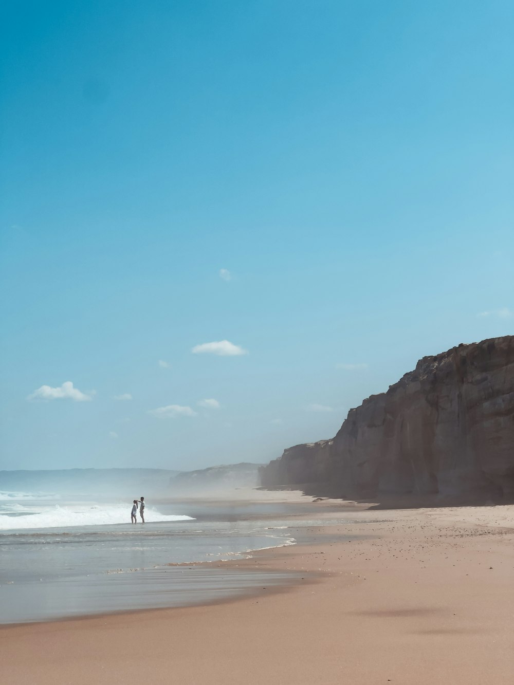 two people standing on a beach next to the ocean