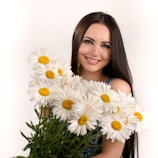 a woman holding a bunch of daisies in her hands