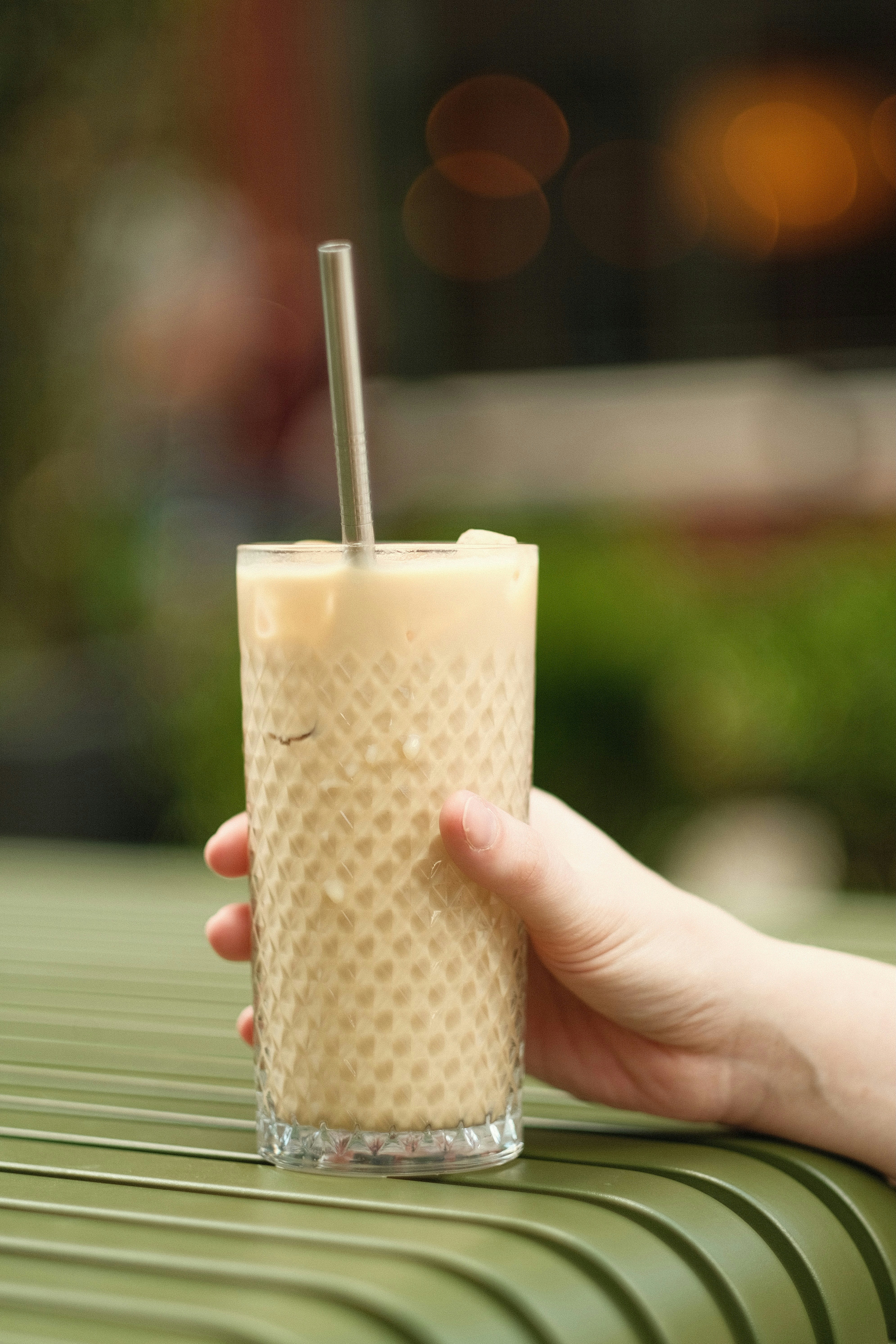a hand holding a drink on top of a green table