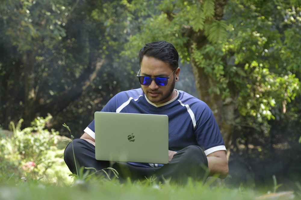 a man sitting in the grass using a laptop computer