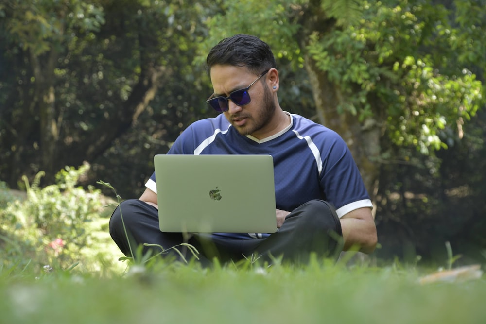 a man sitting in the grass using a laptop computer