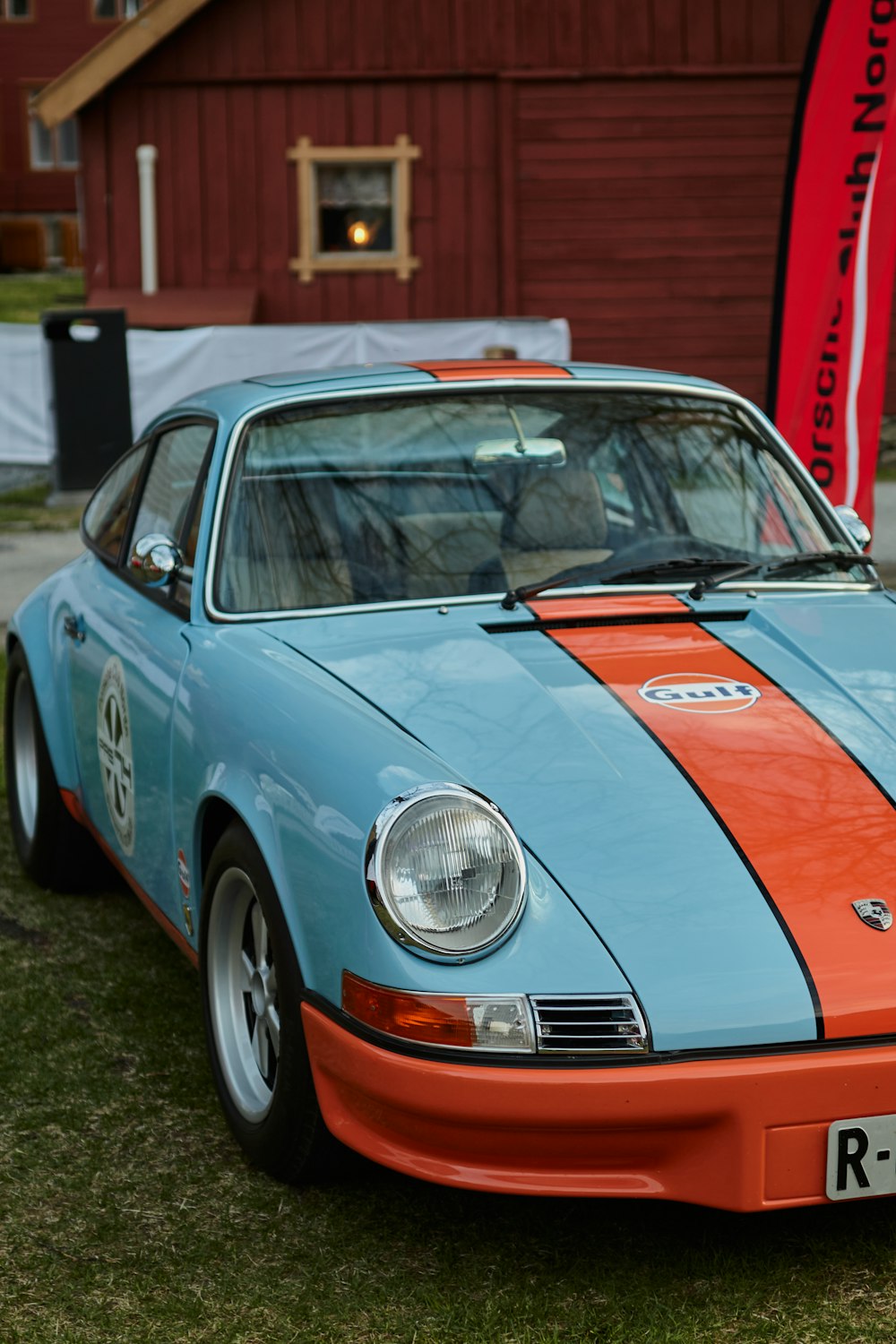 a blue and orange sports car parked in front of a barn