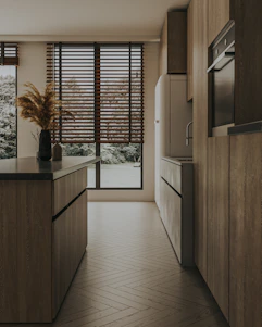 A sunlit, elegant kitchen showcasing handcrafted cabinetry in warm sand tones with natural materials and subtle greenery.