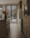 A modern kitchen with sleek wooden cabinets and an island featuring dark countertops. Large windows with wooden blinds allow natural light to filter in, highlighting the warm tones of the wooden floor. A simple arrangement of pampas grass in a vase adds a touch of natural decor.