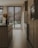 A modern kitchen with sleek wooden cabinets and an island featuring dark countertops. Large windows with wooden blinds allow natural light to filter in, highlighting the warm tones of the wooden floor. A simple arrangement of pampas grass in a vase adds a touch of natural decor.
