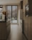 A modern kitchen with sleek wooden cabinets and an island featuring dark countertops. Large windows with wooden blinds allow natural light to filter in, highlighting the warm tones of the wooden floor. A simple arrangement of pampas grass in a vase adds a touch of natural decor.