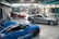 A spacious automotive workshop with polished concrete floors is shown. Three cars, a red one, a blue one, and a silver one, are parked indoors. The background reveals various mechanical equipment and scattered boxes, suggesting ongoing work.