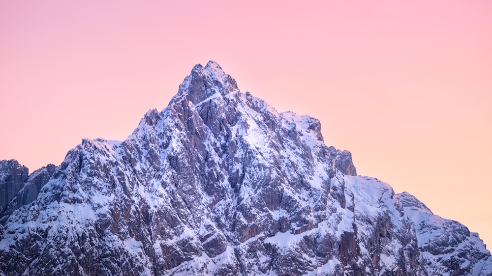 a very tall mountain covered in snow under a pink sky