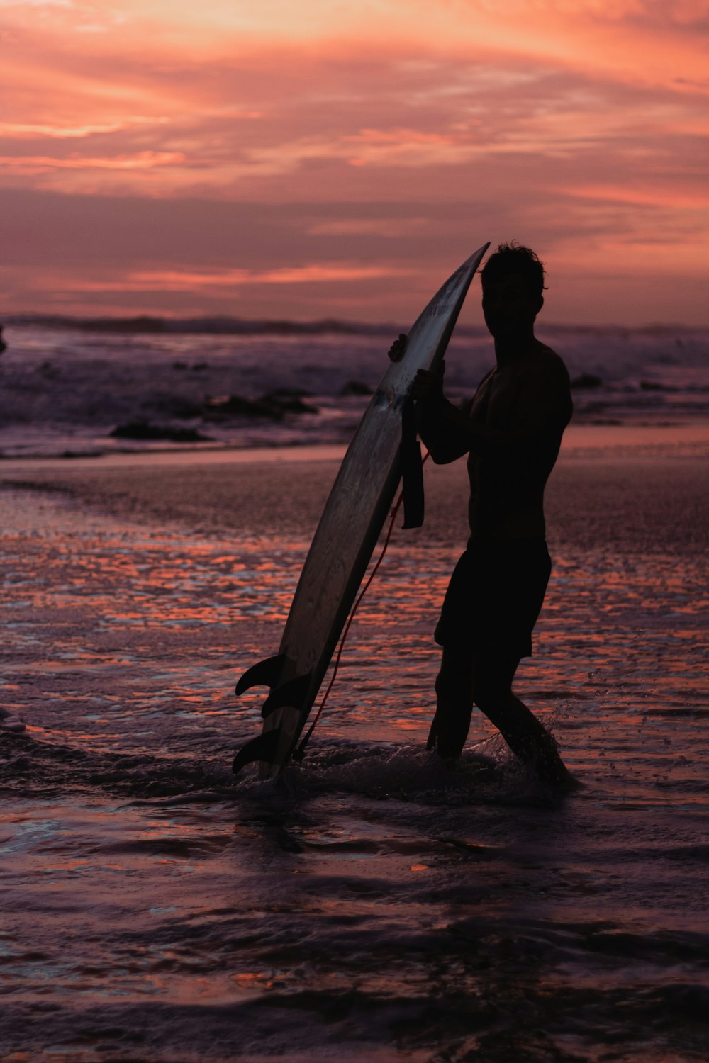 Ein Mann, der bei Sonnenuntergang ein Surfbrett in den Ozean trägt