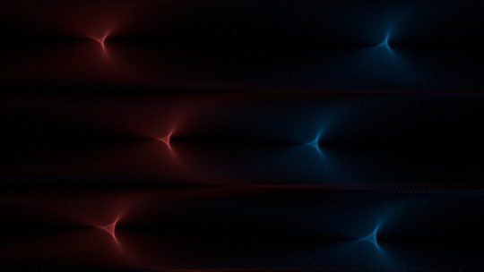 A digital artwork featuring symmetrical, glowing patterns resembling starbursts. The left side displays red hues while the right side shifts to blue, set against a dark background.