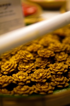 A display of intricately crafted pastries shaped like golden flowers, arranged closely together. The focus is primarily on the textured petals, each with a subtle sheen, hinting at a sophisticated baking technique. The background is softly blurred, adding depth to the foreground arrangement.