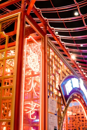 A vibrant neon-lit structure with intricate lattice designs. The neon lights include both bright red and blue colors, with some Asian script visible. The scene reflects a lively, bustling atmosphere often associated with urban nightlife.