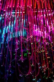 Colorful strands of fiber optic cables cascade downwards, illuminated in vibrant shades of pink, blue, and green. The strands are interspersed with small sparkling lights, creating a dazzling display of light and color.