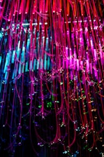 Colorful strands of fiber optic cables cascade downwards, illuminated in vibrant shades of pink, blue, and green. The strands are interspersed with small sparkling lights, creating a dazzling display of light and color.