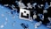 Floating geometric shapes, resembling shattered glass, are suspended around a central logo against a backdrop transitioning from black to blue. The scene conveys a sense of motion and fragmentation.