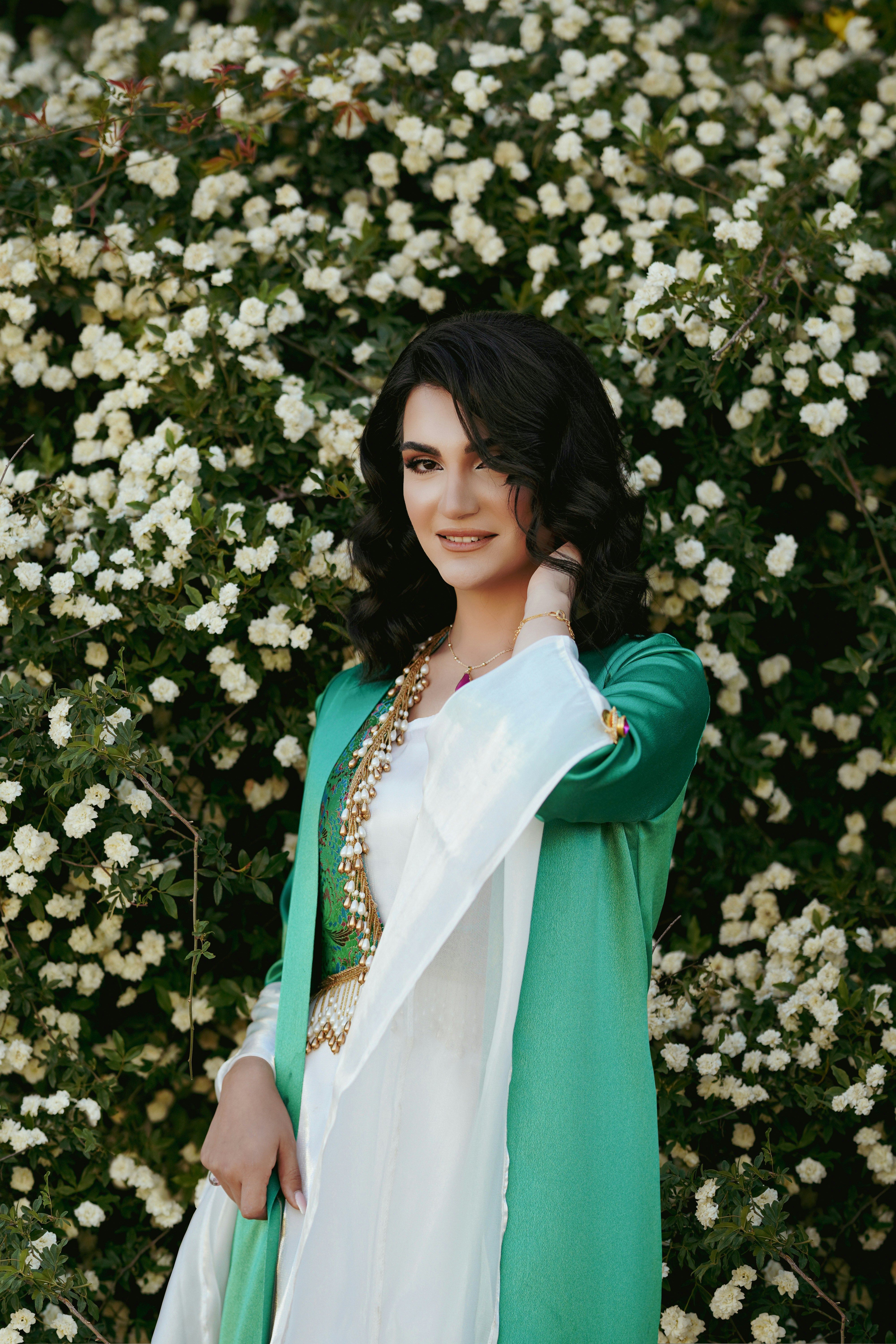 a woman standing in front of a bush with white flowers