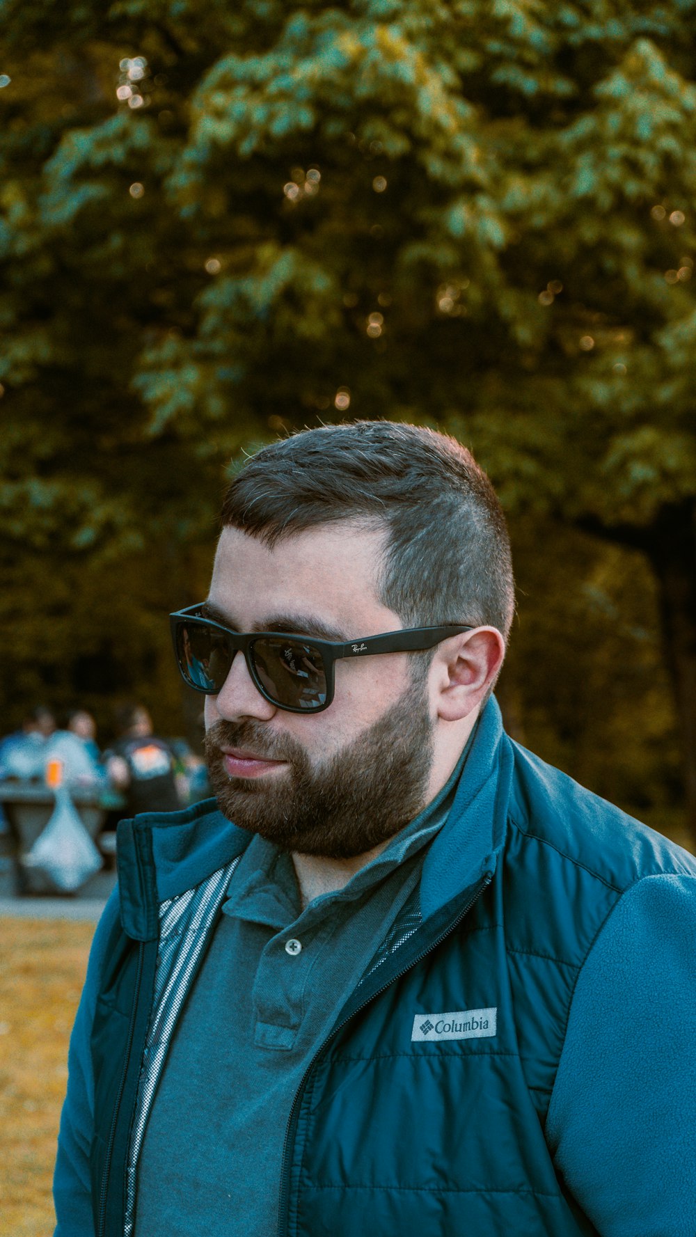 un homme avec une barbe portant des lunettes de soleil et une veste bleue